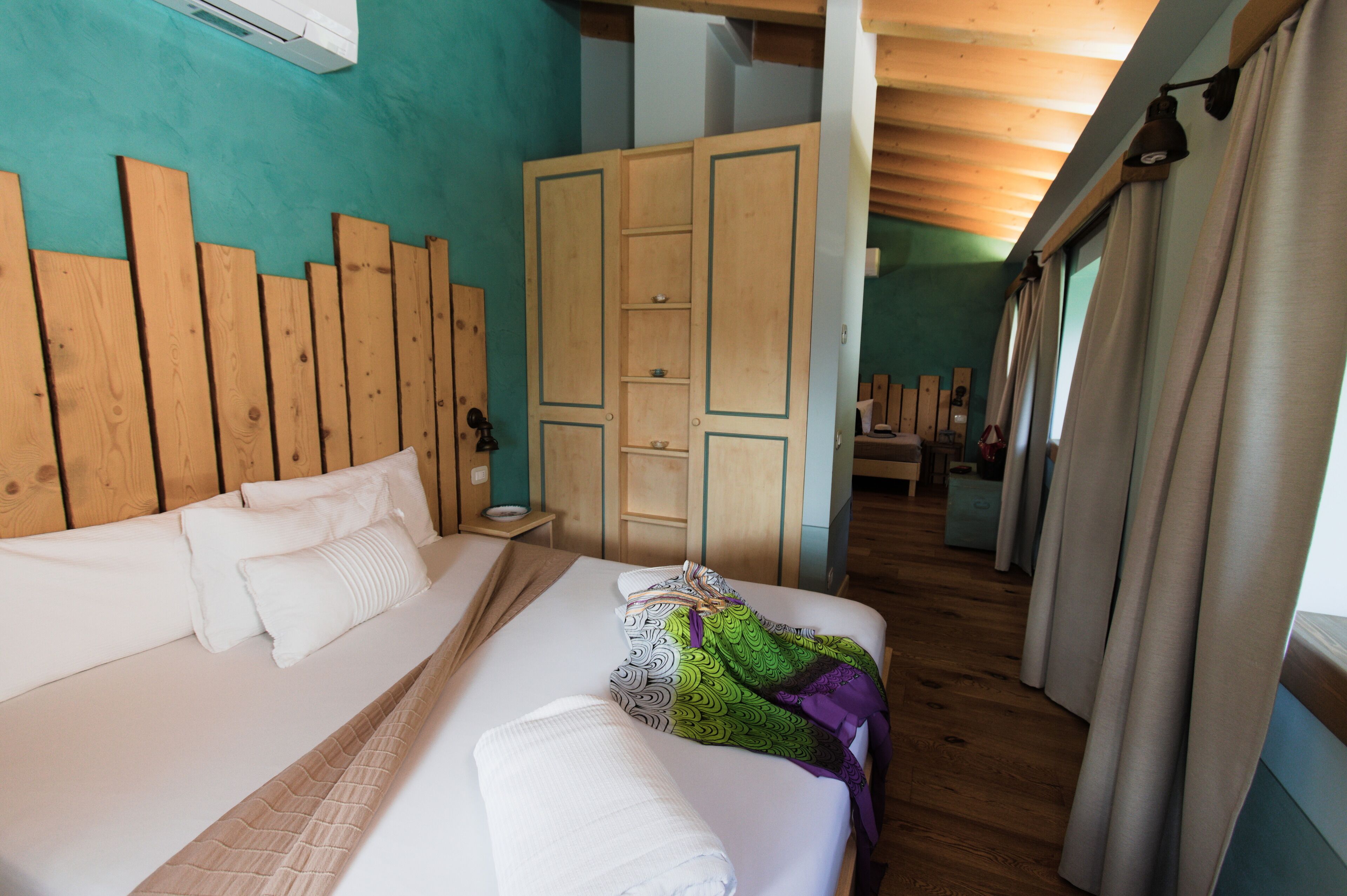 A bedroom with a wooden headboard, a bed with white linens, a green patterned throw, and a wooden wardrobe.