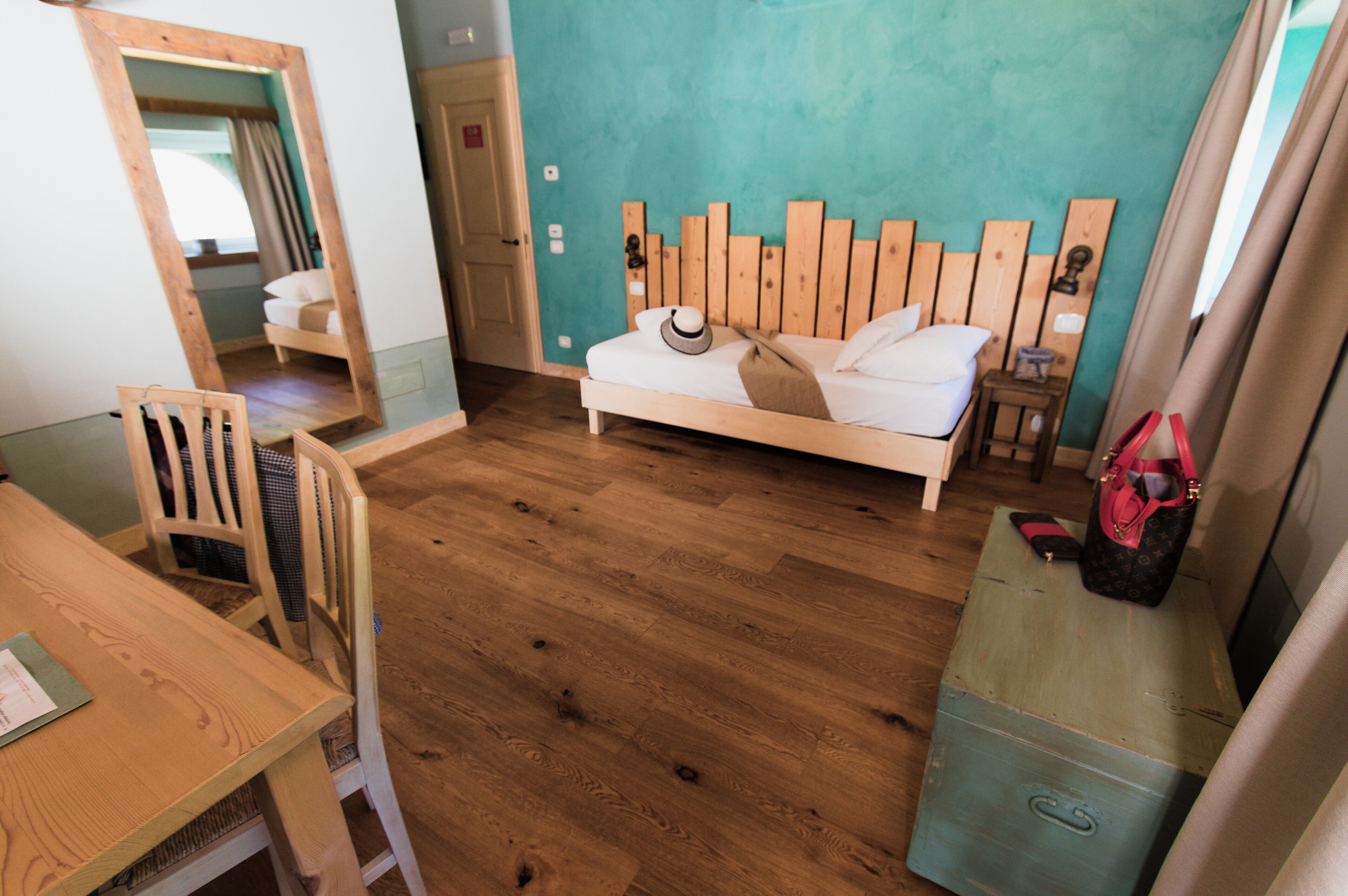 Een slaapkamer met een houten bed, een houten stoel, een klein tafeltje en een koffer.