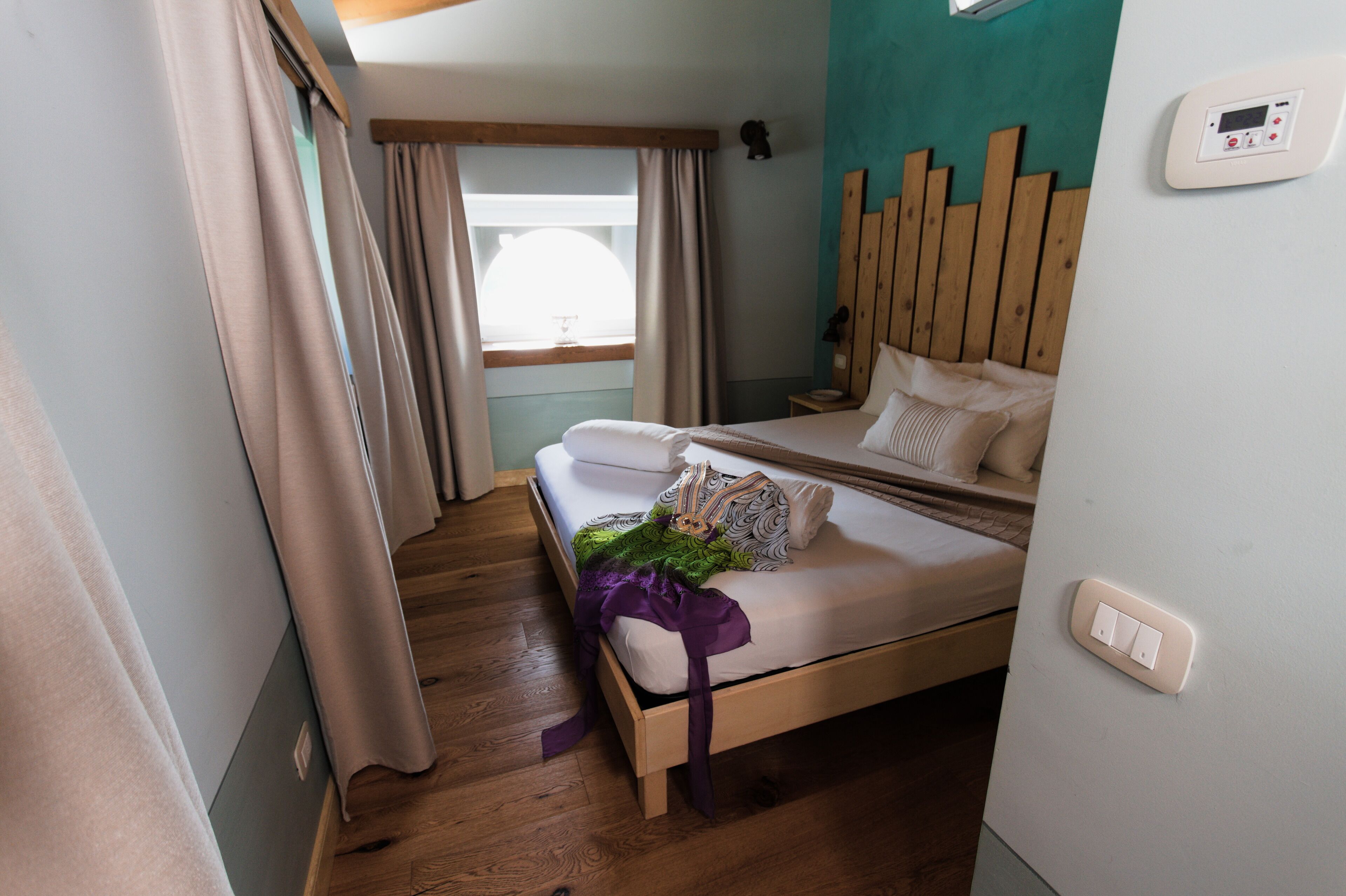 Una habitación de hotel con cama, cortinas, una ventana y un termostato en la pared.