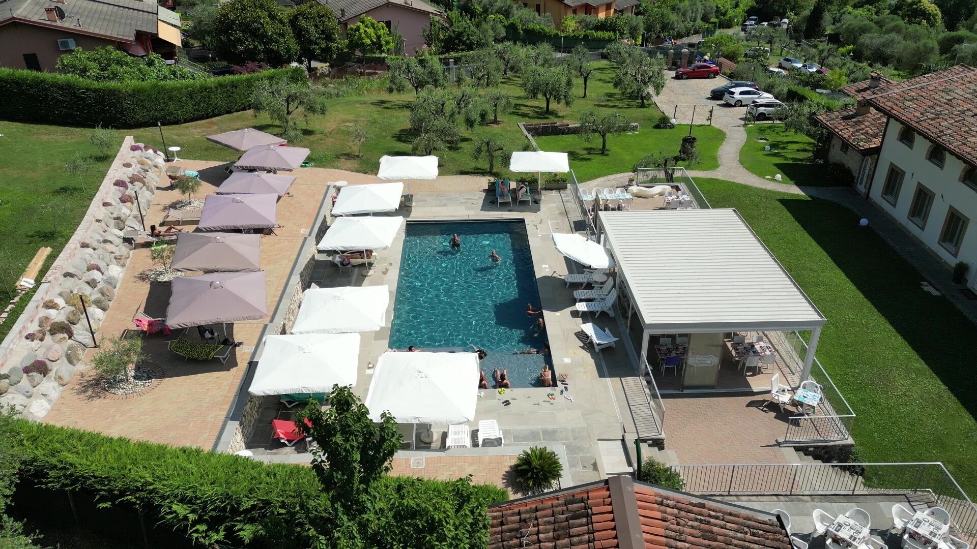 An aerial view of a resort with a central swimming pool, sun loungers, and umbrellas.