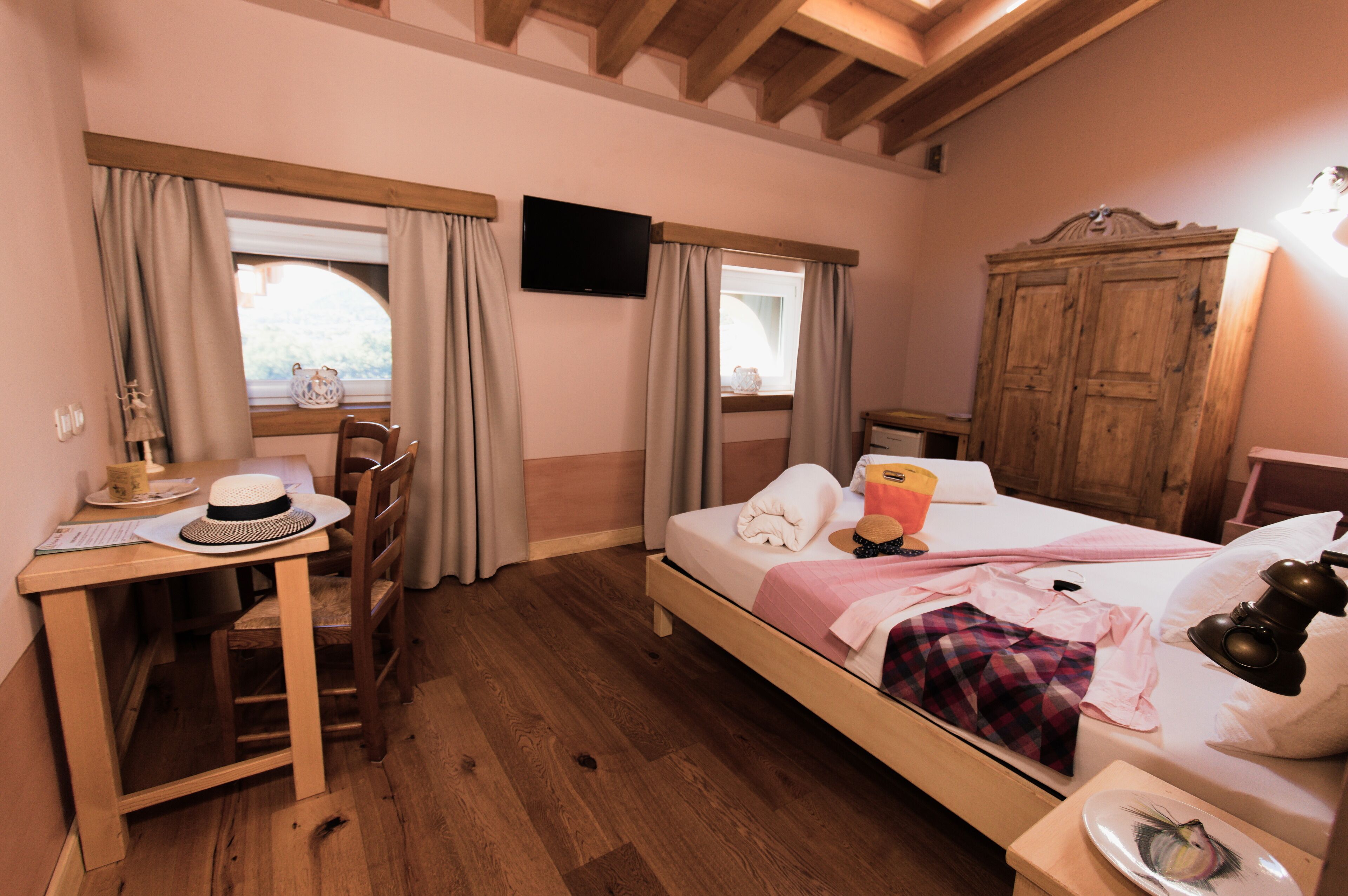 Ein Hotelzimmer mit einem hölzernen Bett, einem Schreibtisch mit Stuhl, einem Fernseher und einem Kleiderschrank.
