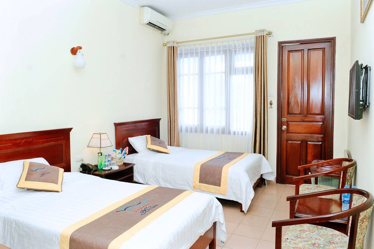 Une chambre d’hôtel avec deux lits, un bureau, une chaise, une télévision et une porte.