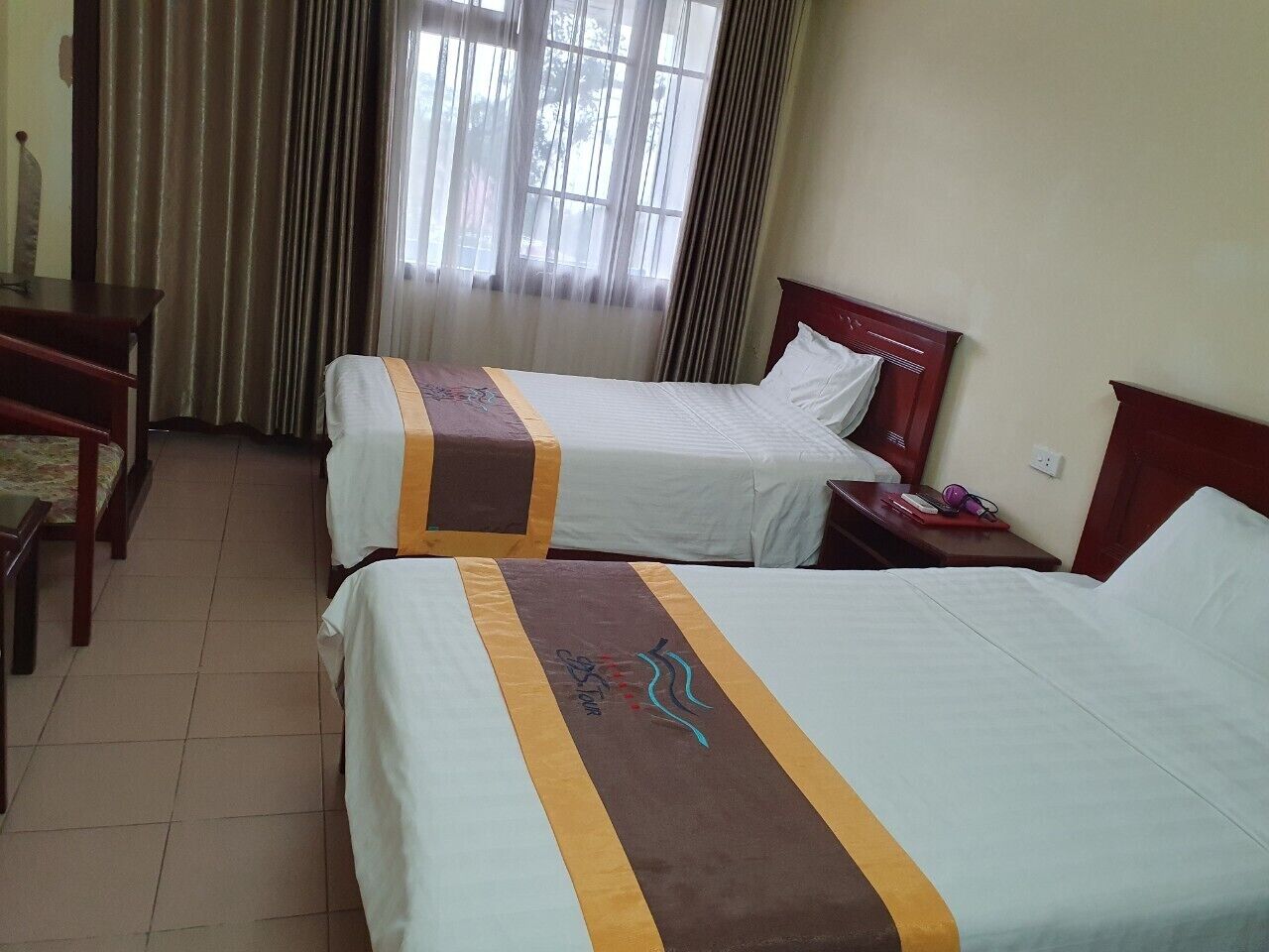 A hotel room with two beds, a wooden desk, and a chair.