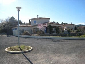 A residential area with a house featuring a tiled roof, a small garden with flowering plants, and a street lamp. - Les S Sens du Sud (Saint-Laurent-de-la-Cabrerisse)