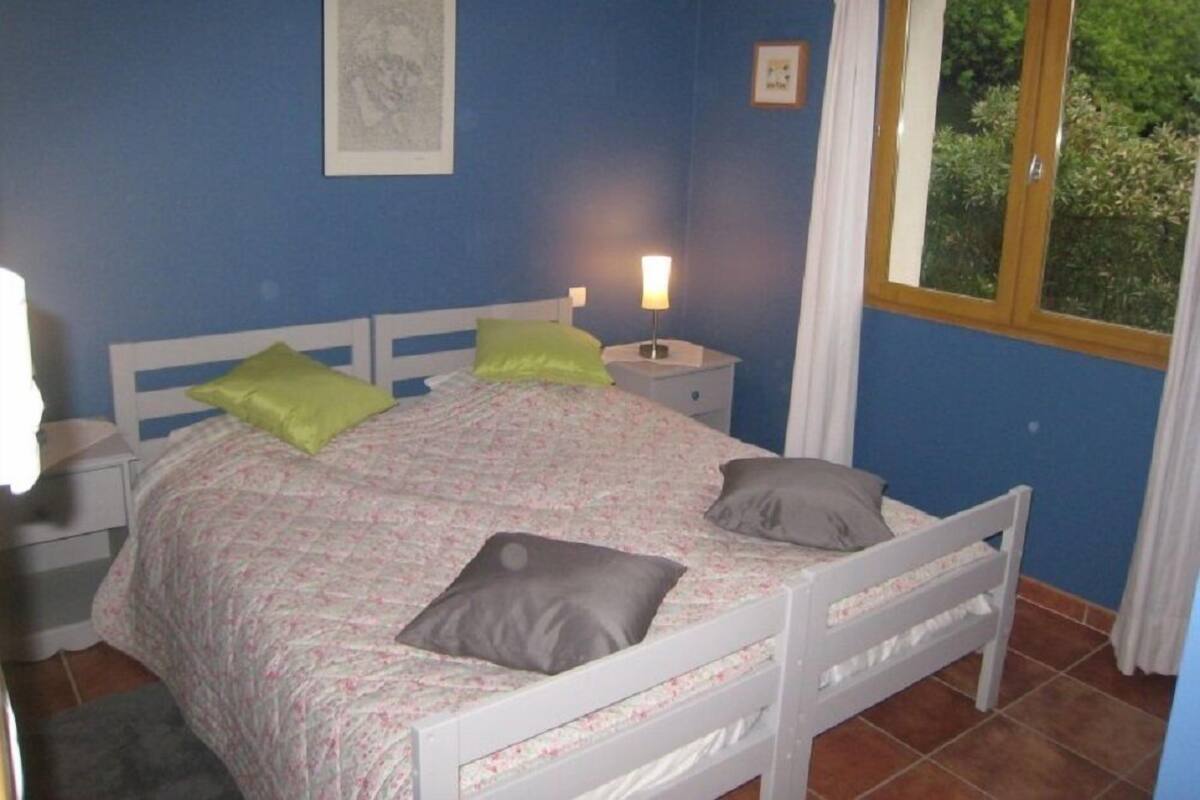 Een slaapkamer met een bed, twee nachtkastjes, een raam met gordijnen en een lijst met een afbeelding aan de muur.