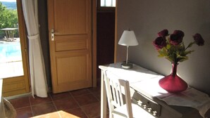Une pièce avec une porte en bois, une table blanche avec une lampe et un vase rempli de fleurs.
