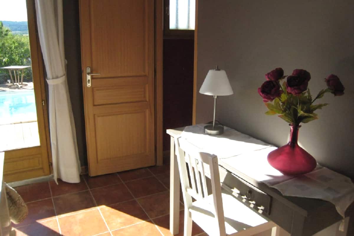 Een kamer met een houten deur, een witte tafel met een lamp en een vaas met bloemen.
