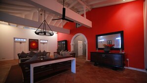 Un salon spacieux avec un plafond haut, un grand ensemble de canapés, une table à manger et un téléviseur posé sur un meuble.