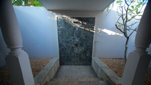 Une pièce aux murs de pierre, dotée d’une petite porte, de piliers blancs et d’un arbre à l’extérieur.