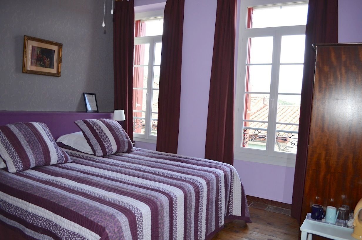 A bedroom with a bed, a window with curtains, a framed picture on the wall, and a wooden wardrobe.