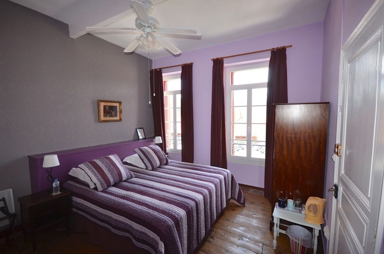 A bedroom with a bed, a nightstand, a desk, a chair, a wardrobe, and a ceiling fan.
