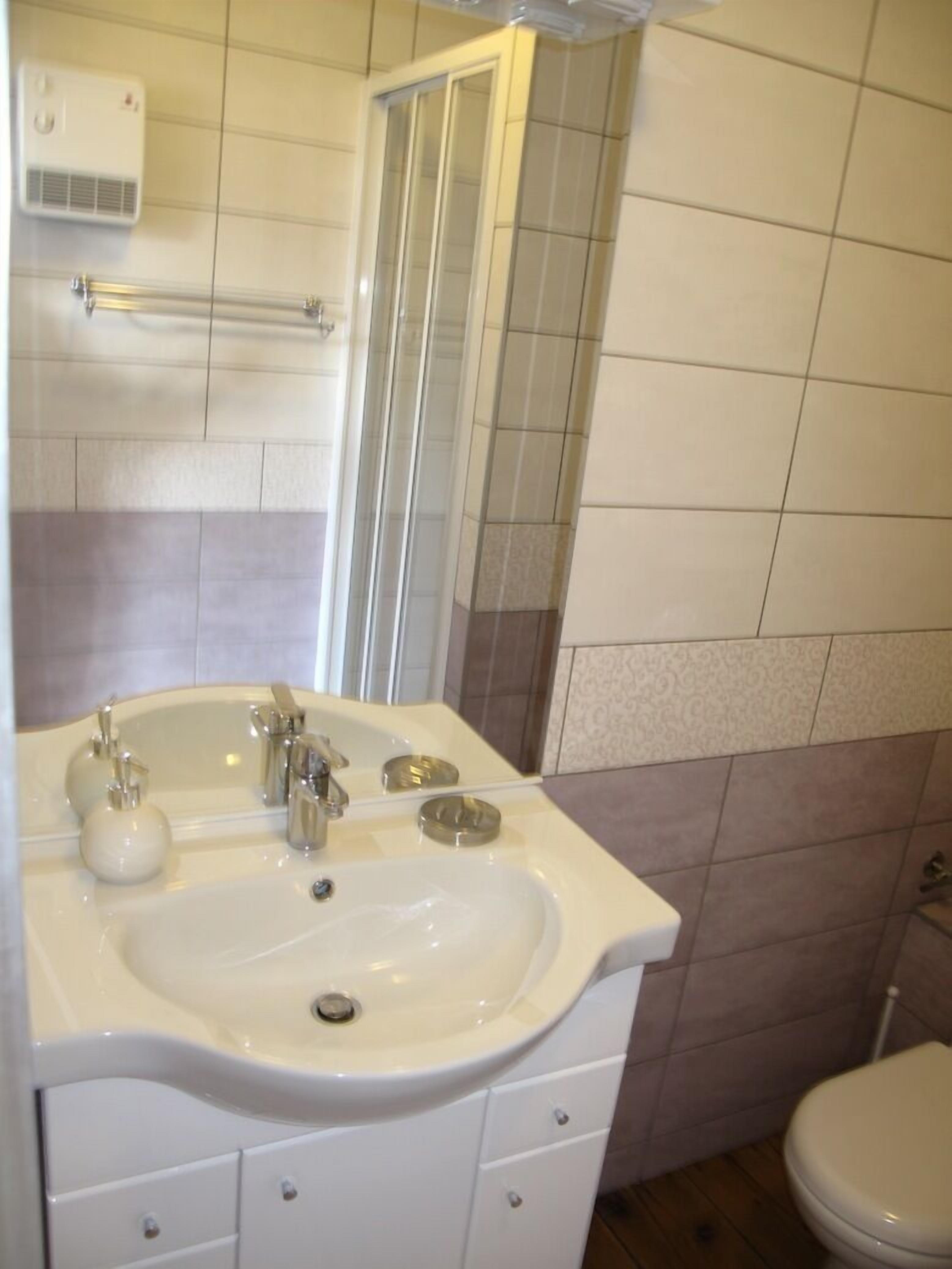 A bathroom with a white sink, two faucets, a mirror, a towel rack, and a toilet.