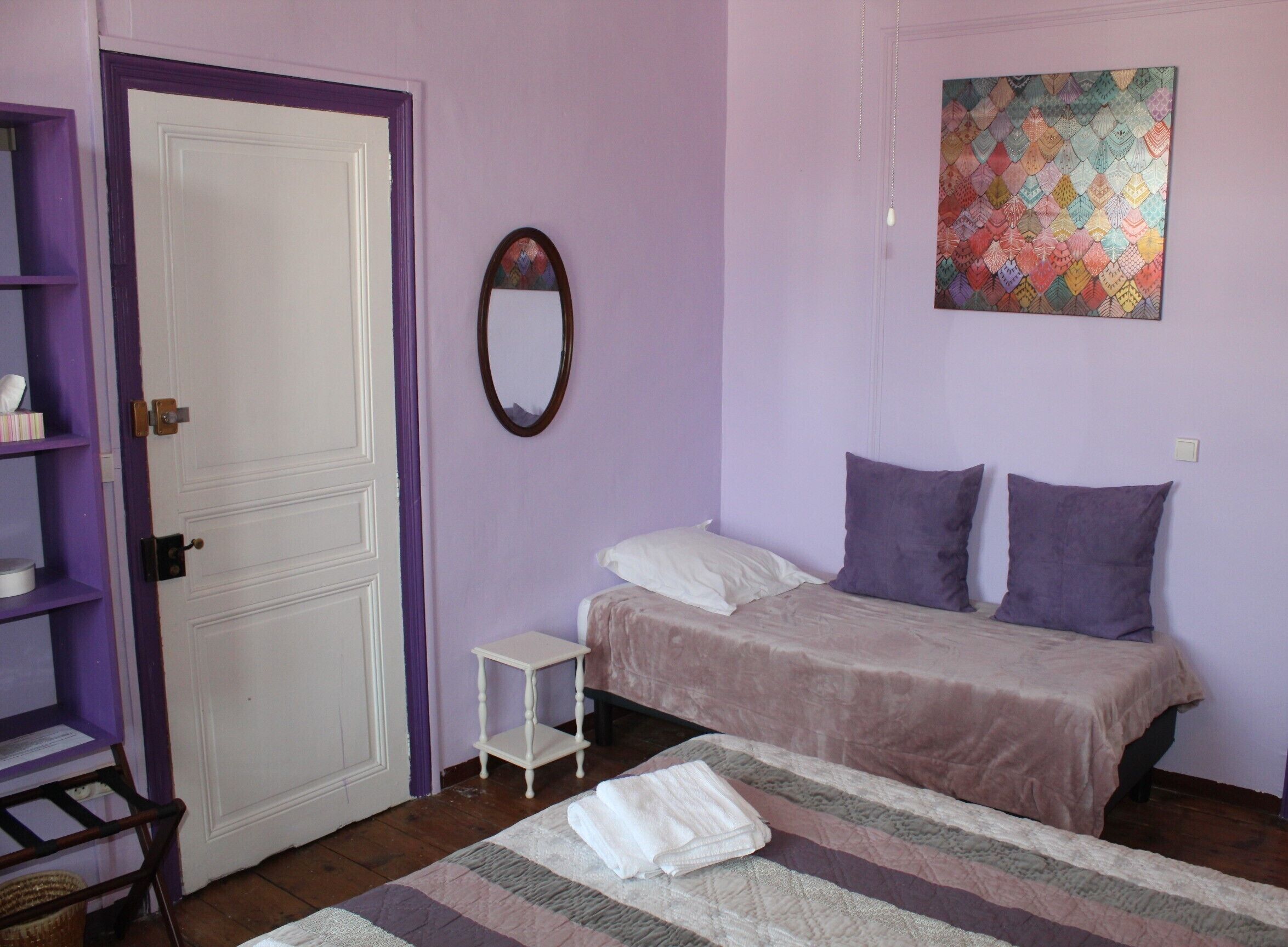 Une chambre à coucher avec un lit, une petite table de chevet, un miroir et une œuvre d’art colorée accrochée au mur.