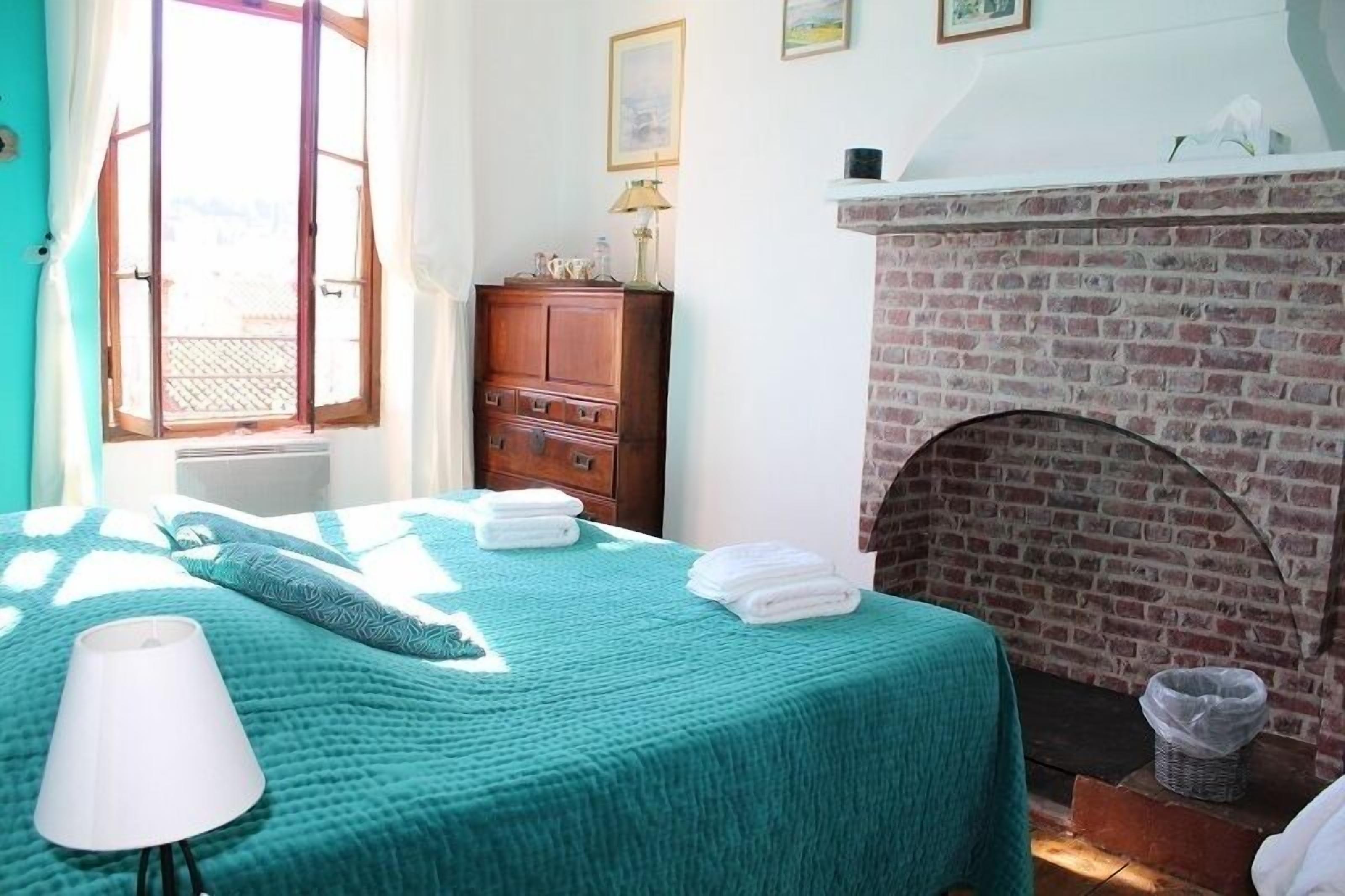 Una habitación con cama, cómoda de madera, chimenea y ventana con cortinas.