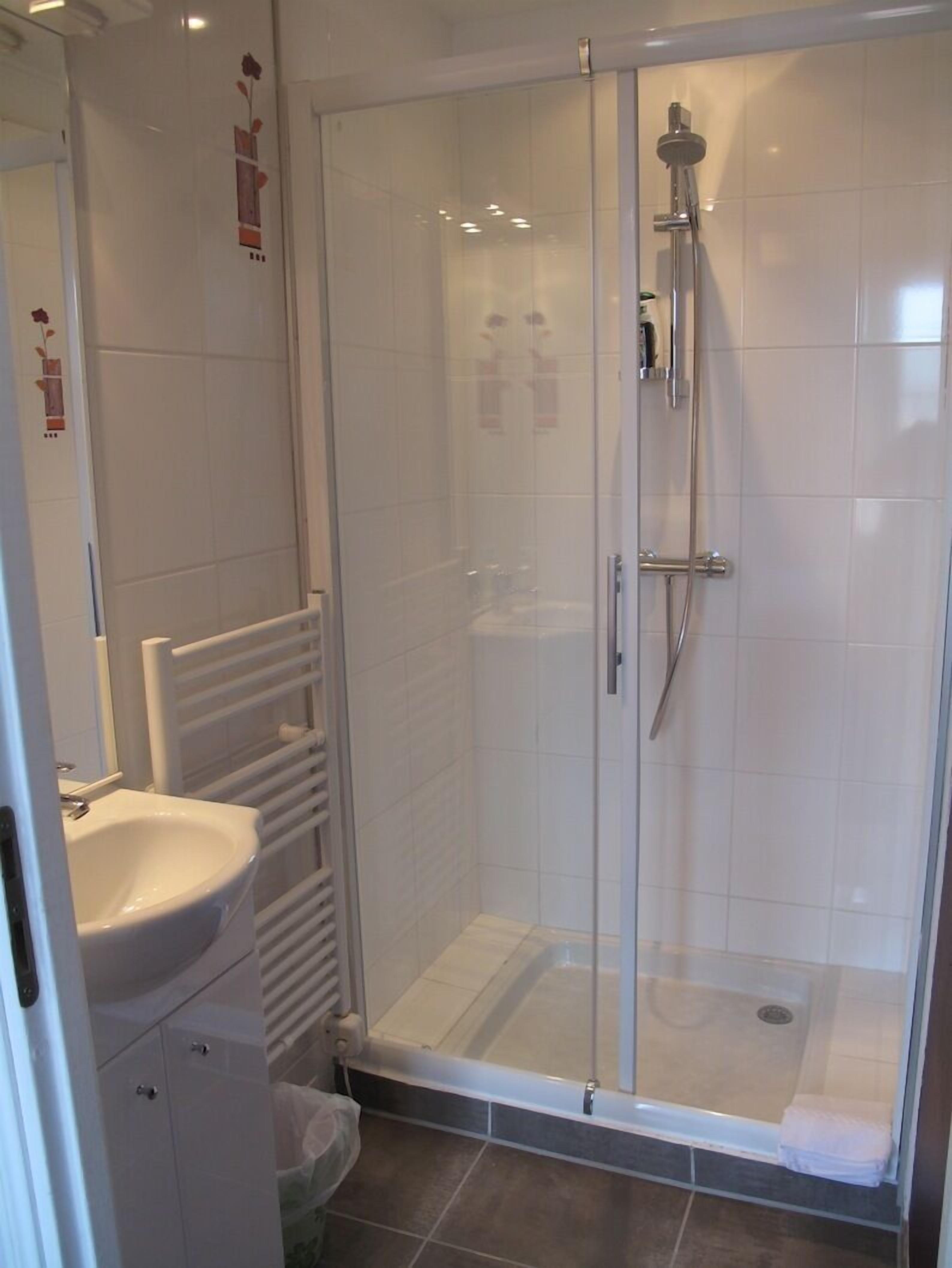 A modern bathroom with a glass-enclosed shower, a white sink, and a towel rack.