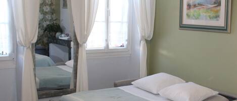 A single bed with a metal frame, white bedding, and a window with curtains.
