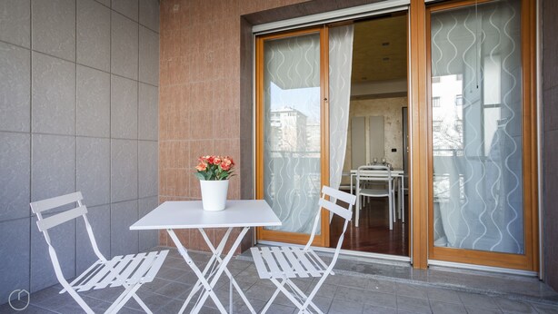 A balcony with a white table and chairs, a potted plant, and a sliding glass door leading to an interior space. - Italianway   - Spadolini 6 (Milan)
