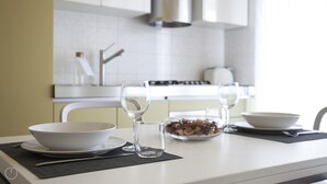 A modern kitchen with white cabinets, a stainless steel range hood, and a dining table set with a bowl, two wine glasses, and a glass jar of nuts. - Italianway   - Spadolini 6 (Milan)