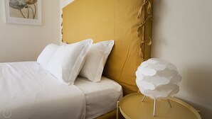 A bed with white bedding, a mustard-colored headboard, and a white decorative sphere on a small table. - Italianway   - Spadolini 6 (Milan)