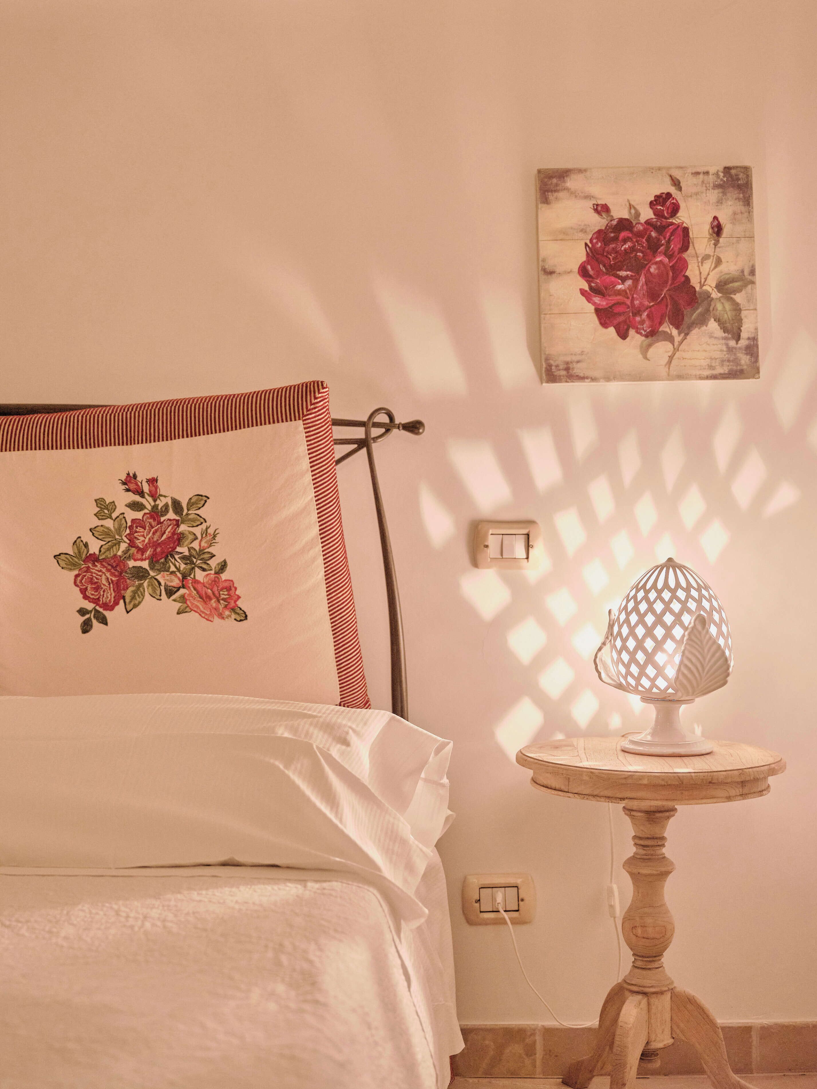 Un lit avec un coussin à motifs floraux, une table de chevet avec une lampe et un interrupteur fixé au mur.