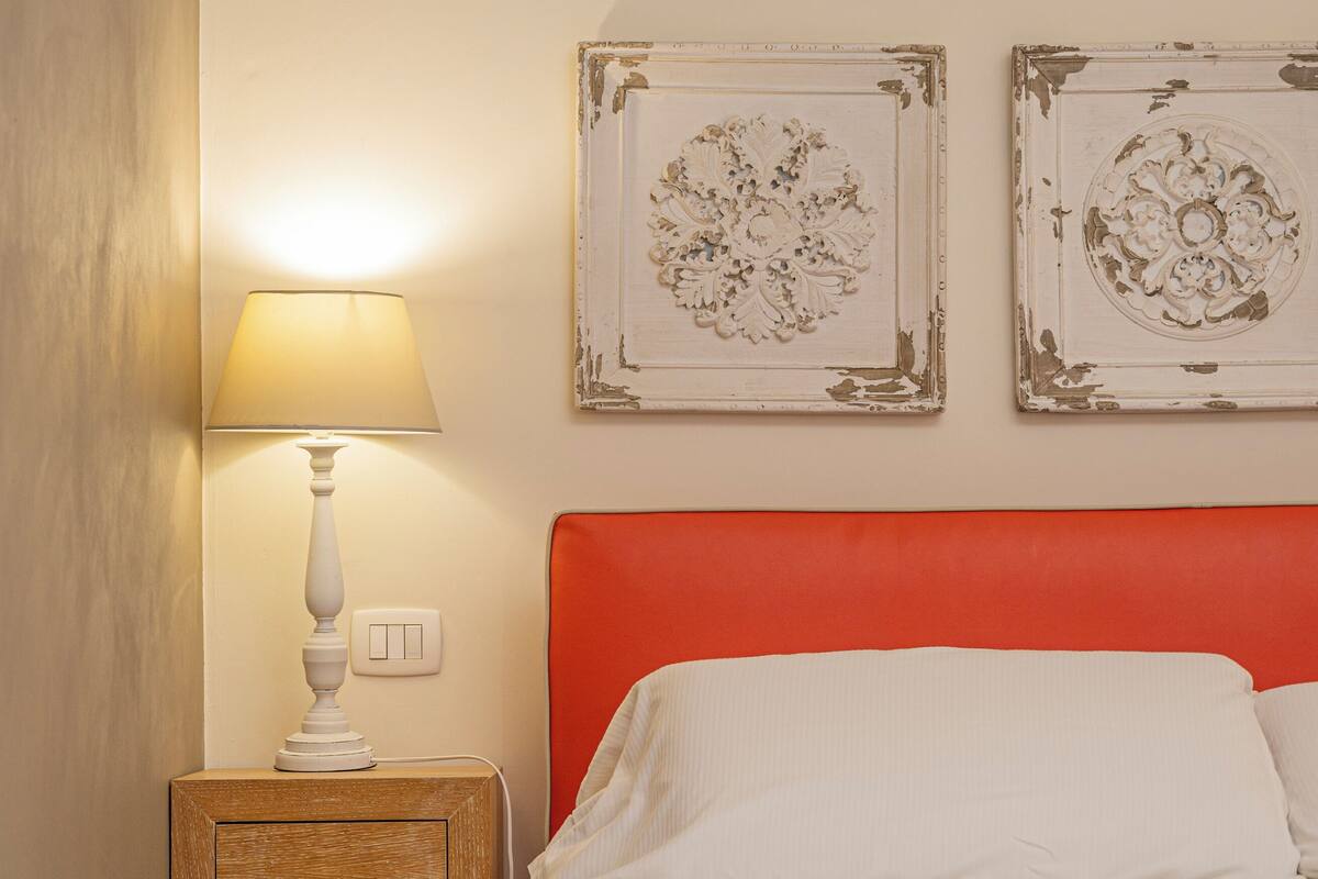 Un lit bien fait, avec une tête de lit rouge, une table de chevet avec une lampe et deux éléments décoratifs accrochés au mur.