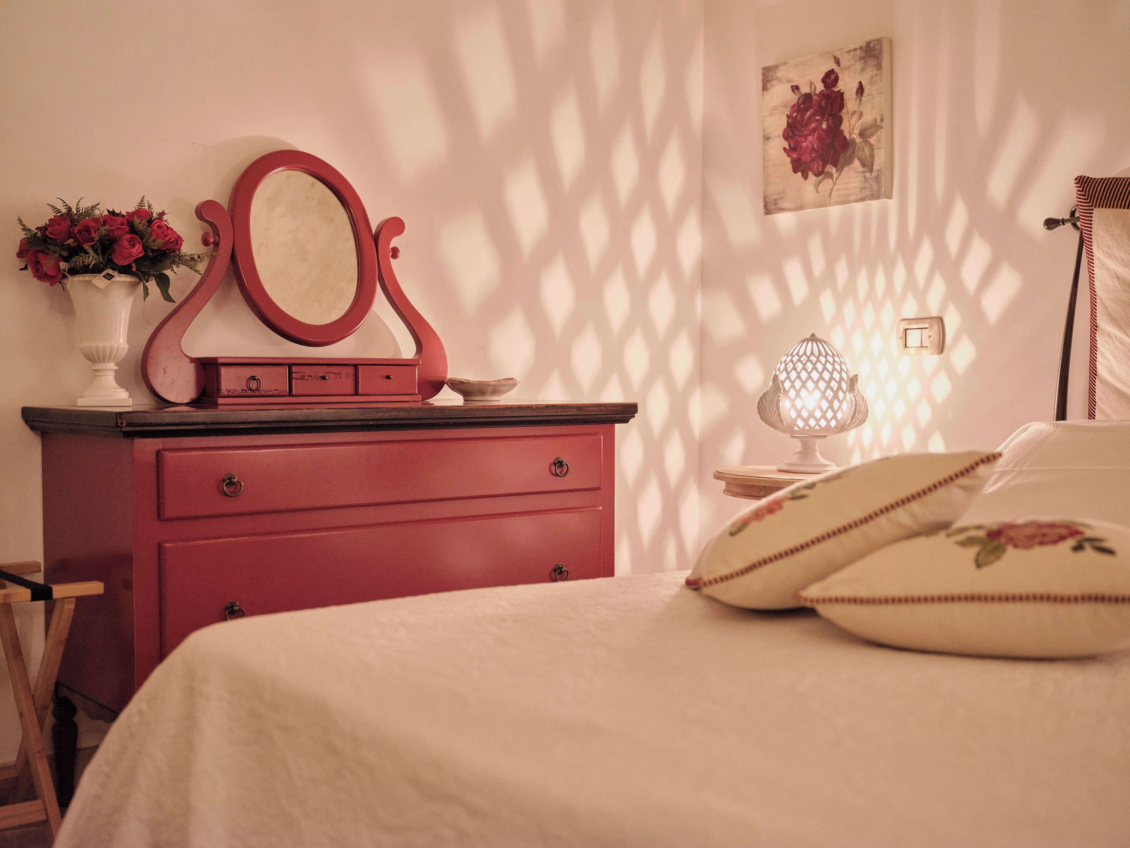A bedroom with a bed, a dresser with a mirror, a vase of flowers, and a lamp.