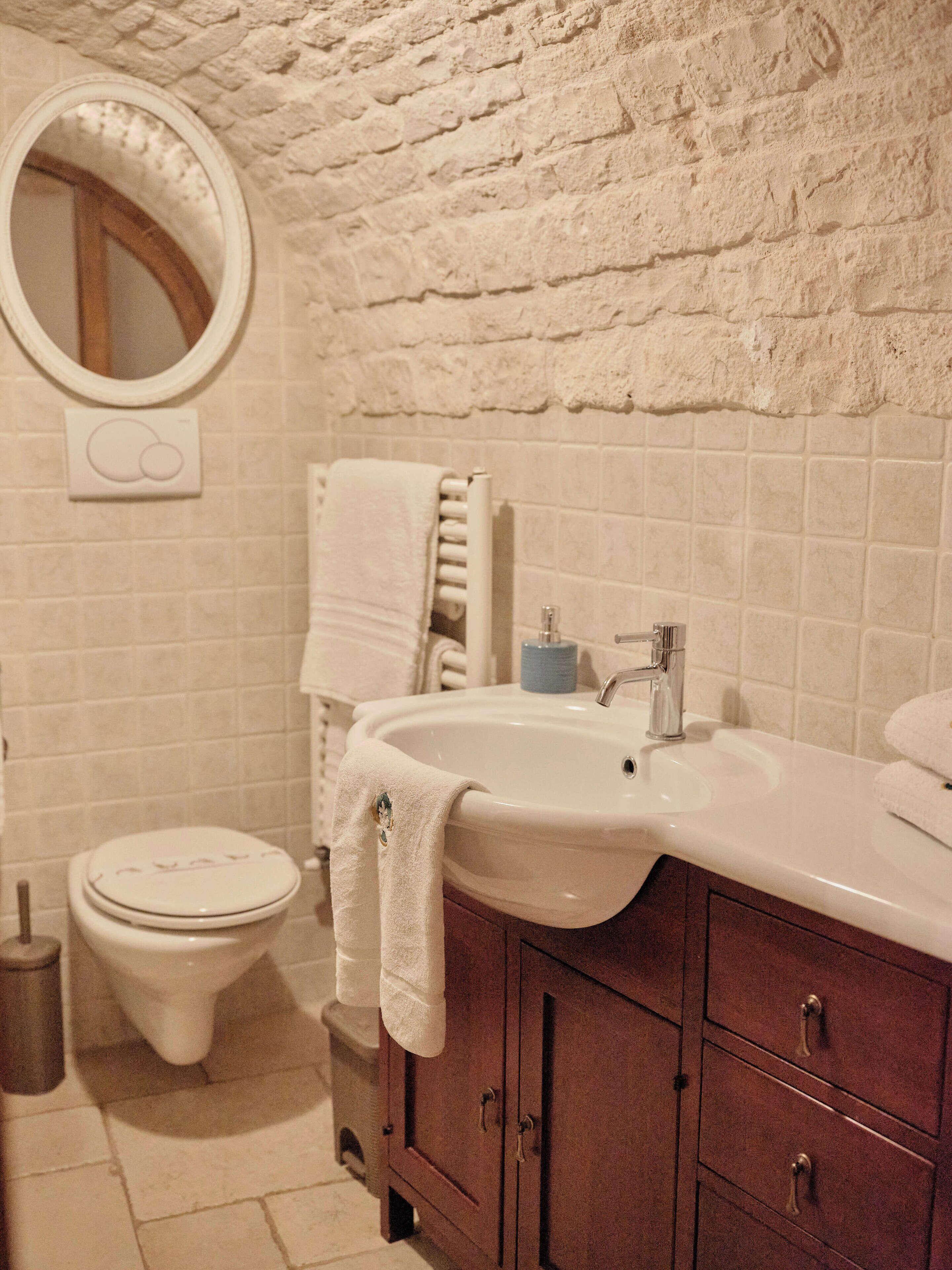 Casa de banho com lavatório branco, espelho, sanita e um porta-toalhas.