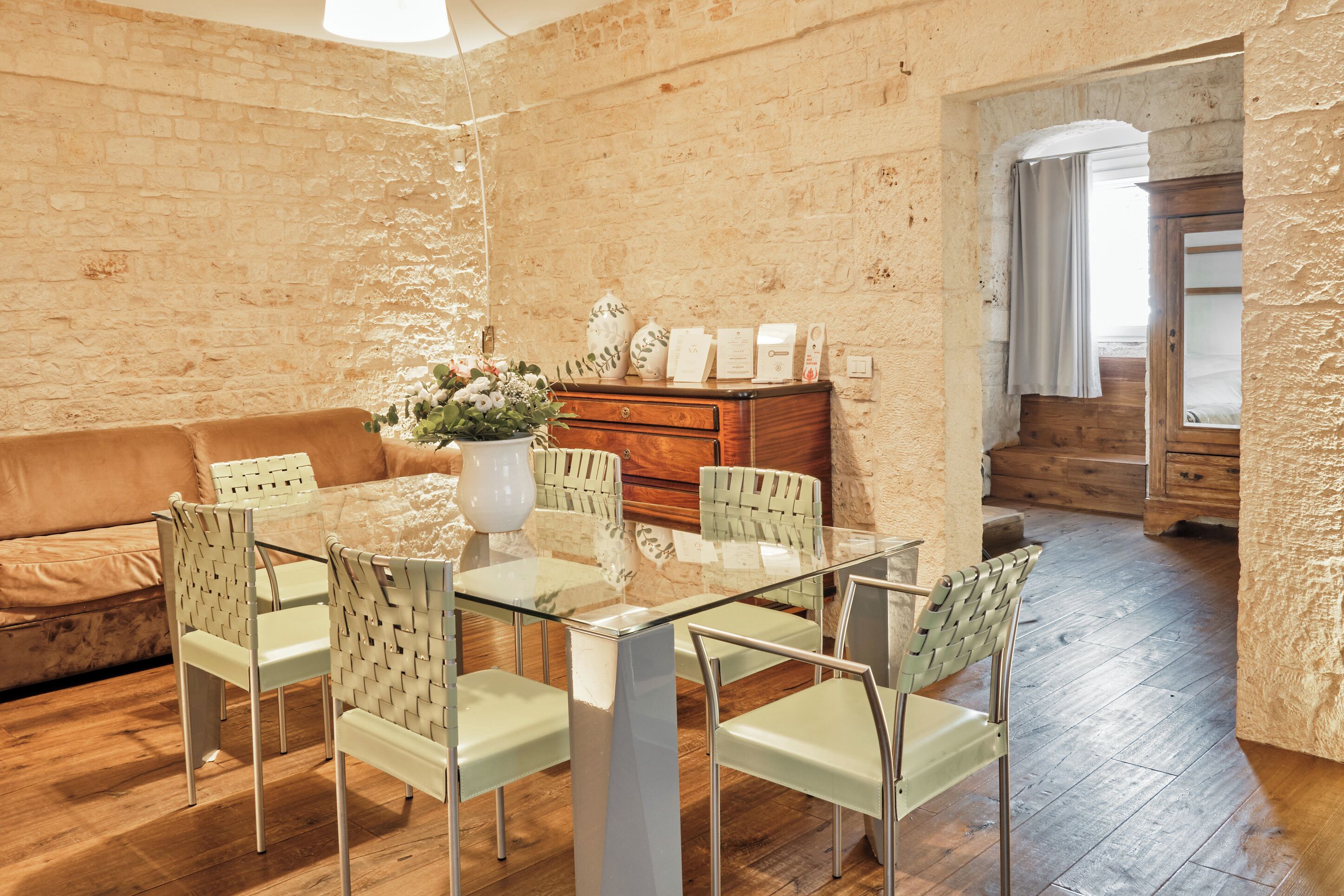 Un coin repas comprenant une table en verre, six chaises, un vase avec des fleurs et un buffet en bois.