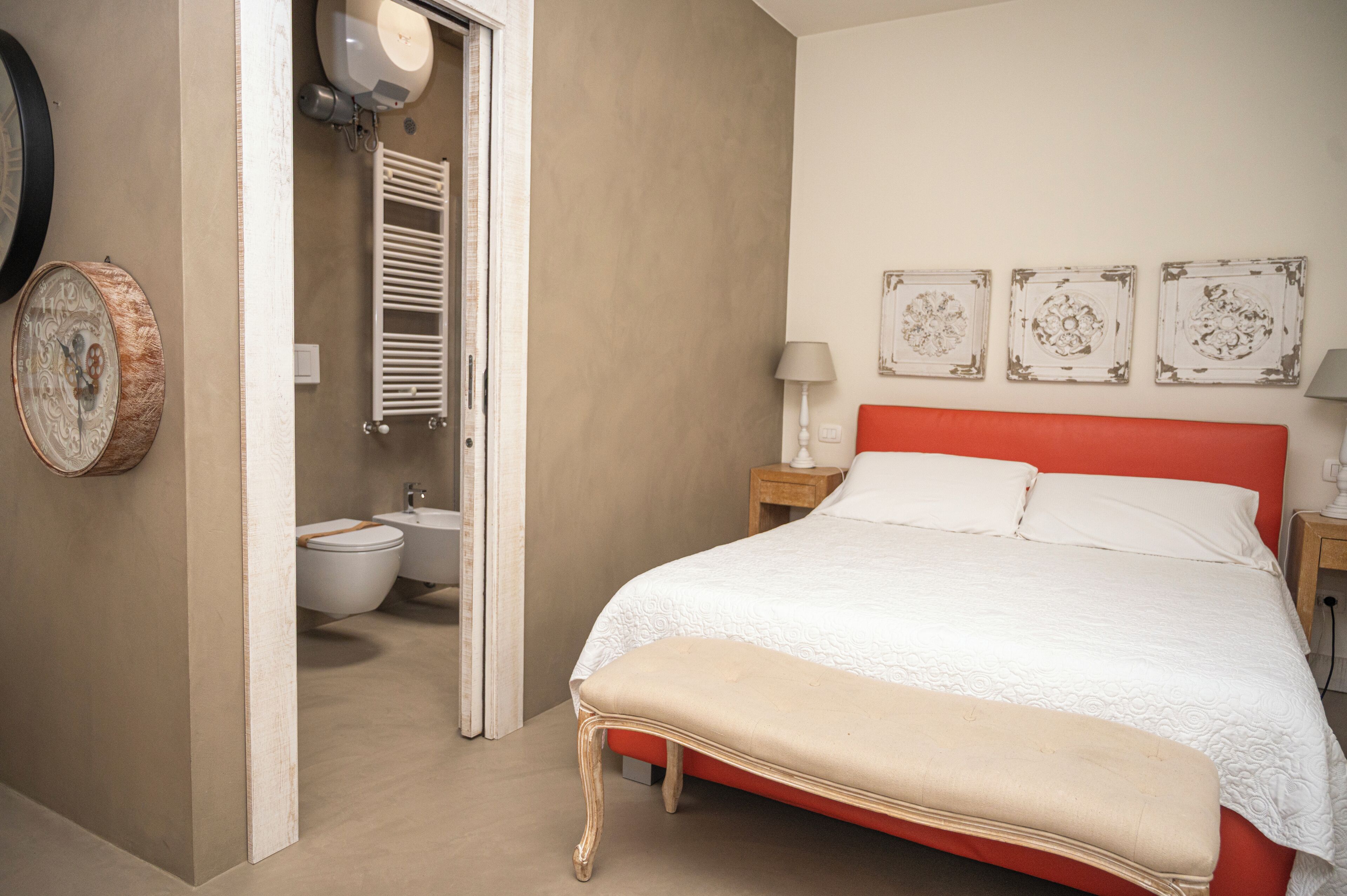 Une chambre à coucher avec une tête de lit rouge, une couvre-lit blanche et un banc en bois.