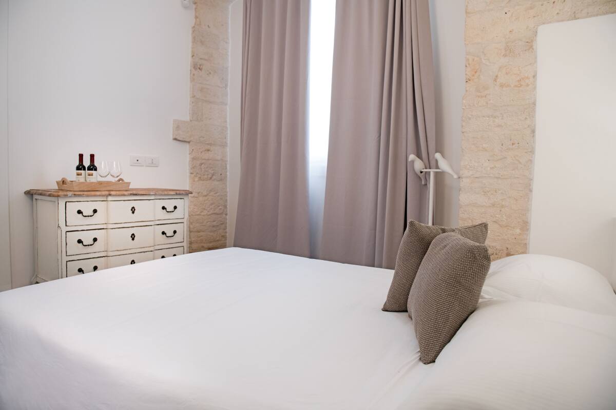Un lit bien fait, avec du linge de lit blanc et deux oreillers marron, une commode avec des tiroirs et une fenêtre avec des rideaux.