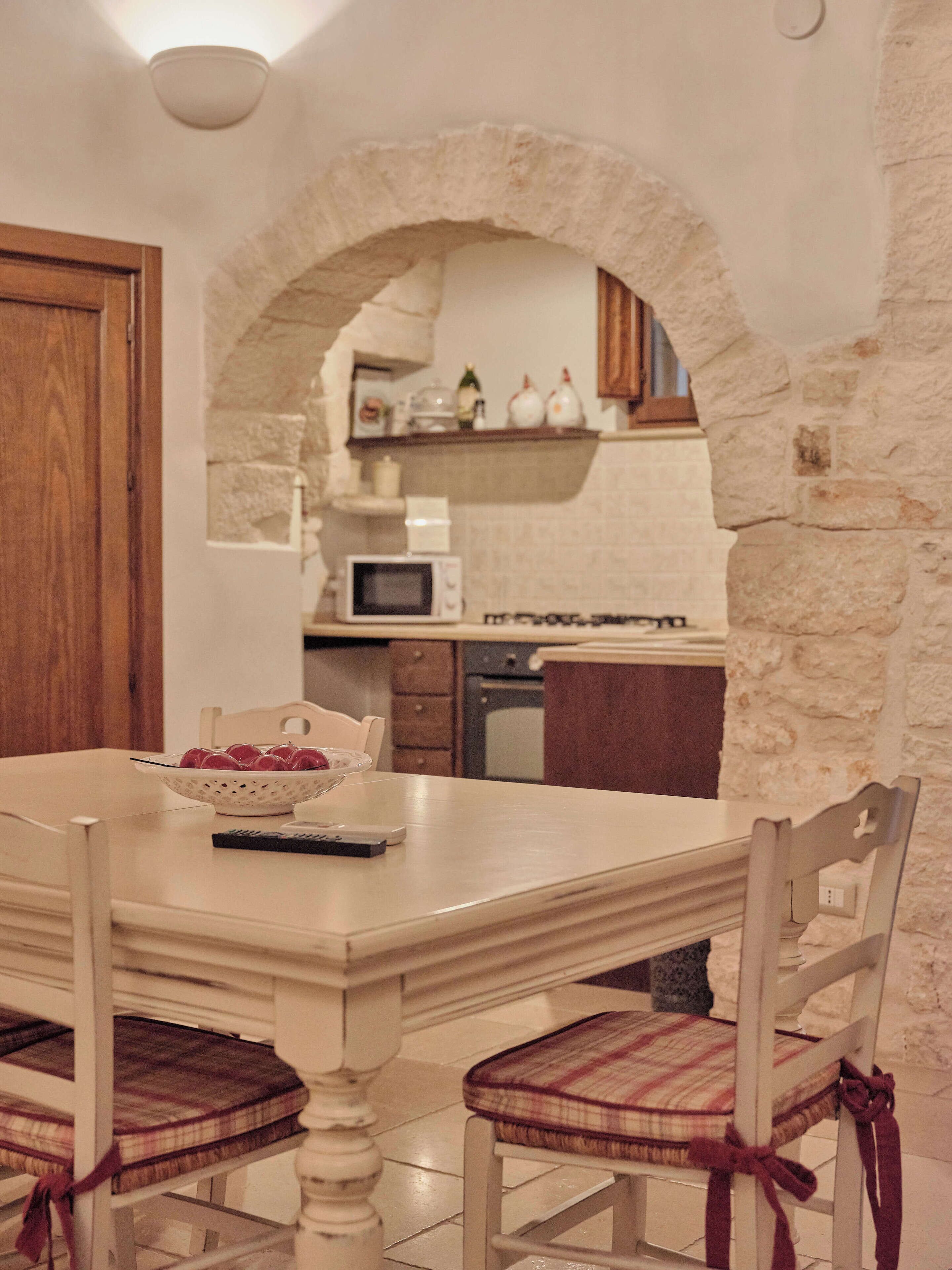 A dining area with a white table, two plaid chairs, and a bowl of fruit.