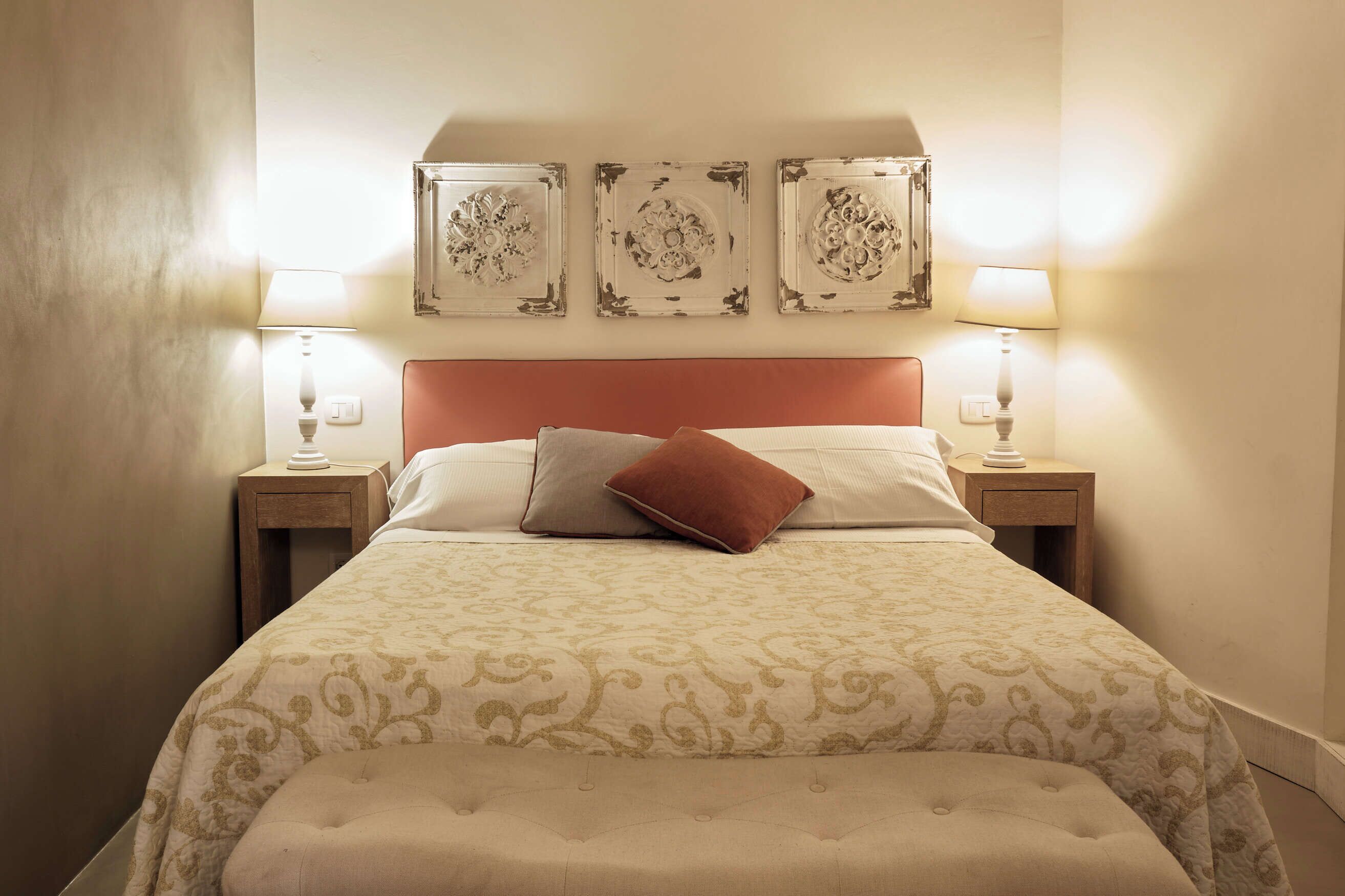 Een netjes opgemaakt bed met een bedsprei met patroon, een rood hoofdeinde en twee bedlampjes.