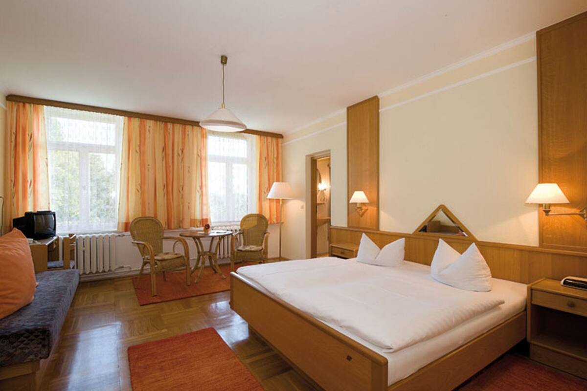 A hotel room with a large bed, a desk with a chair, a television, and a window with curtains.