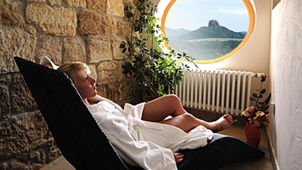 A person reclining in a black chair with a view of a mountain through a circular window. - Panoramahotel Wolfsberg (Reinhardtsdorf-Schoena)