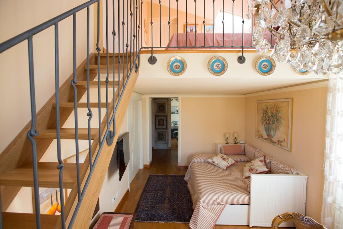 A bedroom with a wooden staircase, a bed with striped bedding, a radiator, and a chandelier.