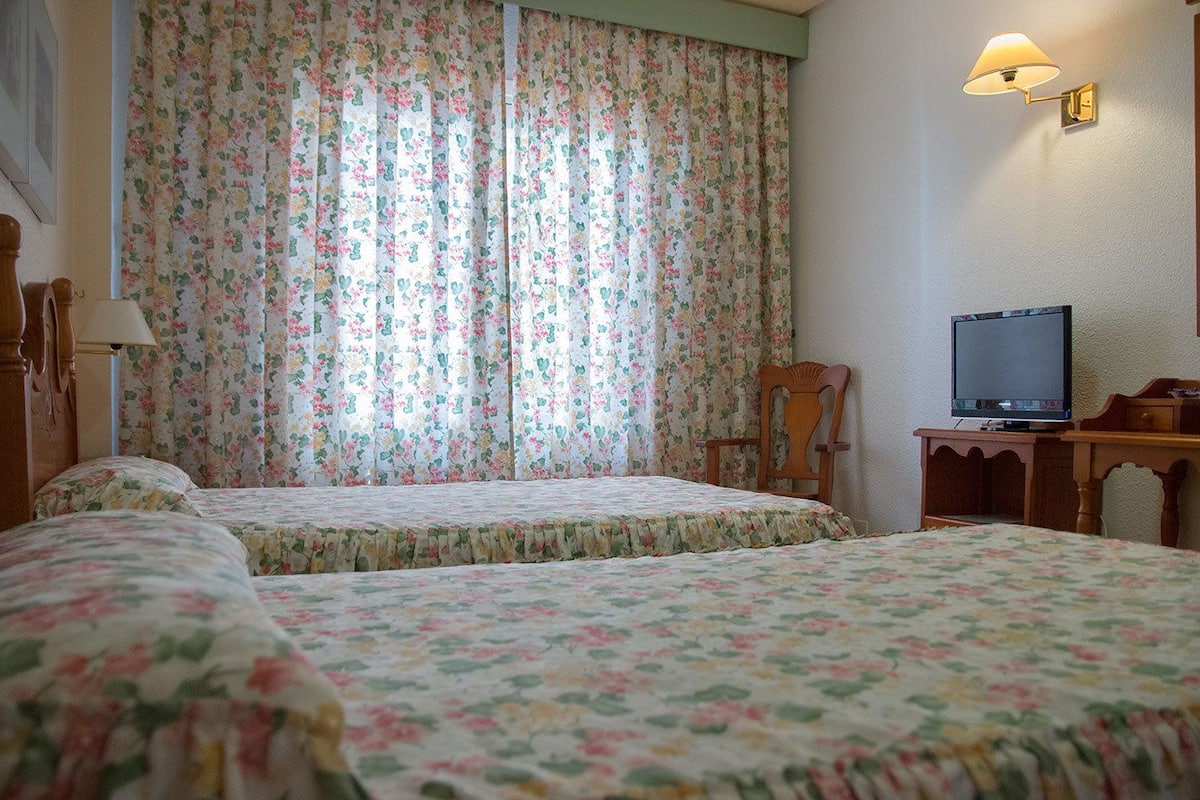 Una habitación con dos camas, televisión y una lámpara.