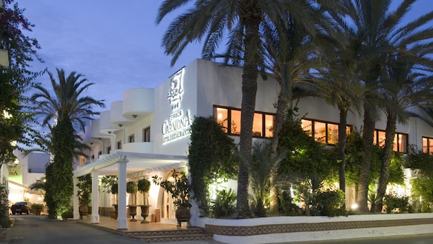 Un hotel con fachada blanca, palmeras y un letrero que dice 'Hotel Carvona'.