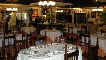 Un restaurante con mesas redondas dispuestas para comer, con manteles blancos y copas de vino ordenadas.