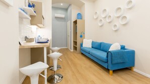 A modern kitchen with white cabinetry, a blue sofa, and a dining area with white chairs. - Budapest Holiday Colours (Budapest)