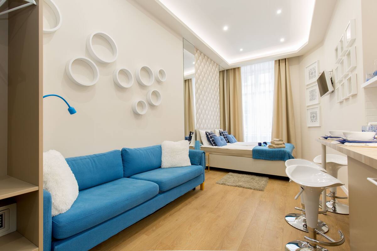 Una sala de estar moderna con un sofá azul, una mesita de centro blanca y una zona de bar con taburetes blancos.