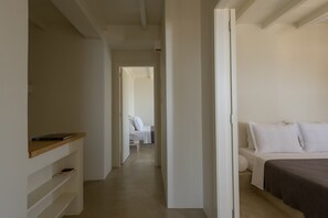 A narrow hallway leading to a bedroom with a bed and a bedside table. - Andros Tessera (Andros)