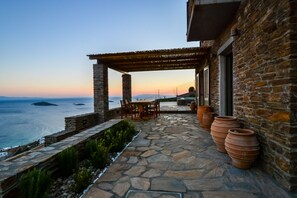 Eine Steinterrasse mit einer Pergola mit Blick aufs Meer, Terrakottatöpfen und einem Tisch mit Stühlen.