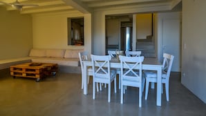 A modern living room with a white sofa, a wooden coffee table, and a dining area with white chairs and a table. - Andros Tessera (Andros)