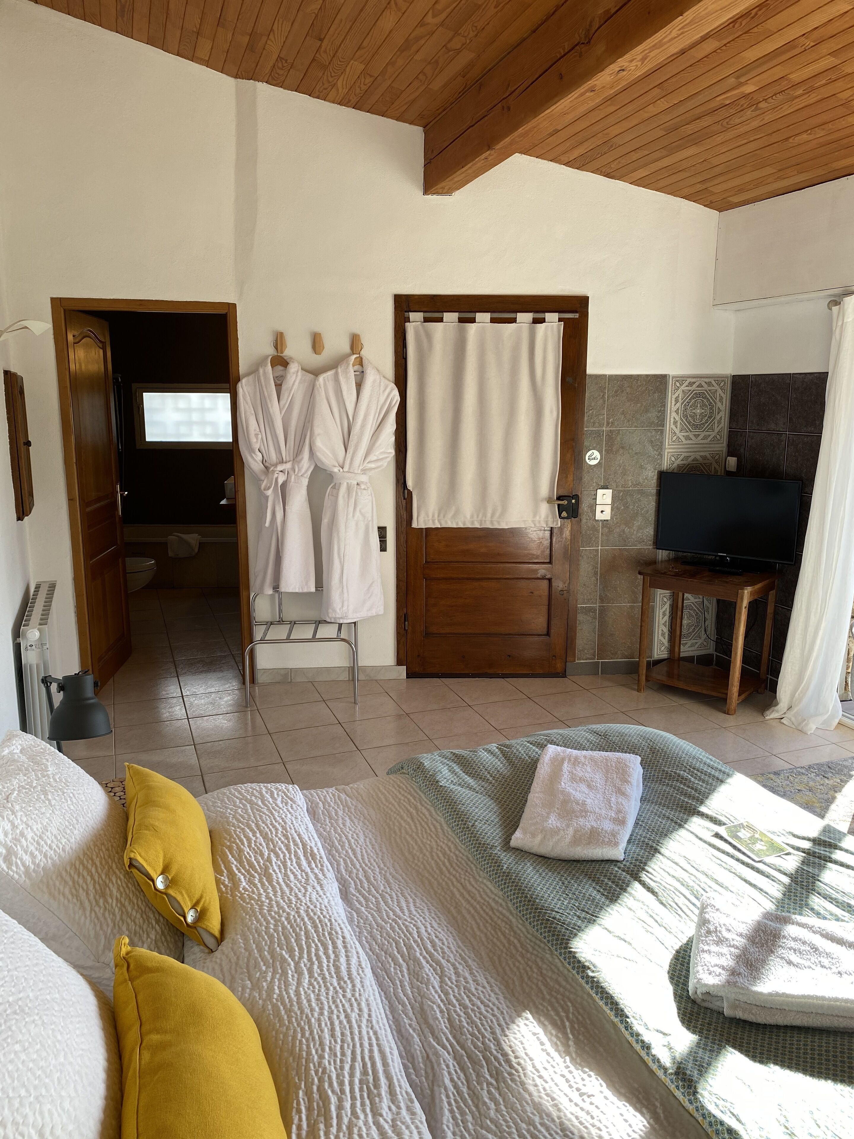 Habitación de hotel con cama, televisor y baño visible a través de una puerta abierta.