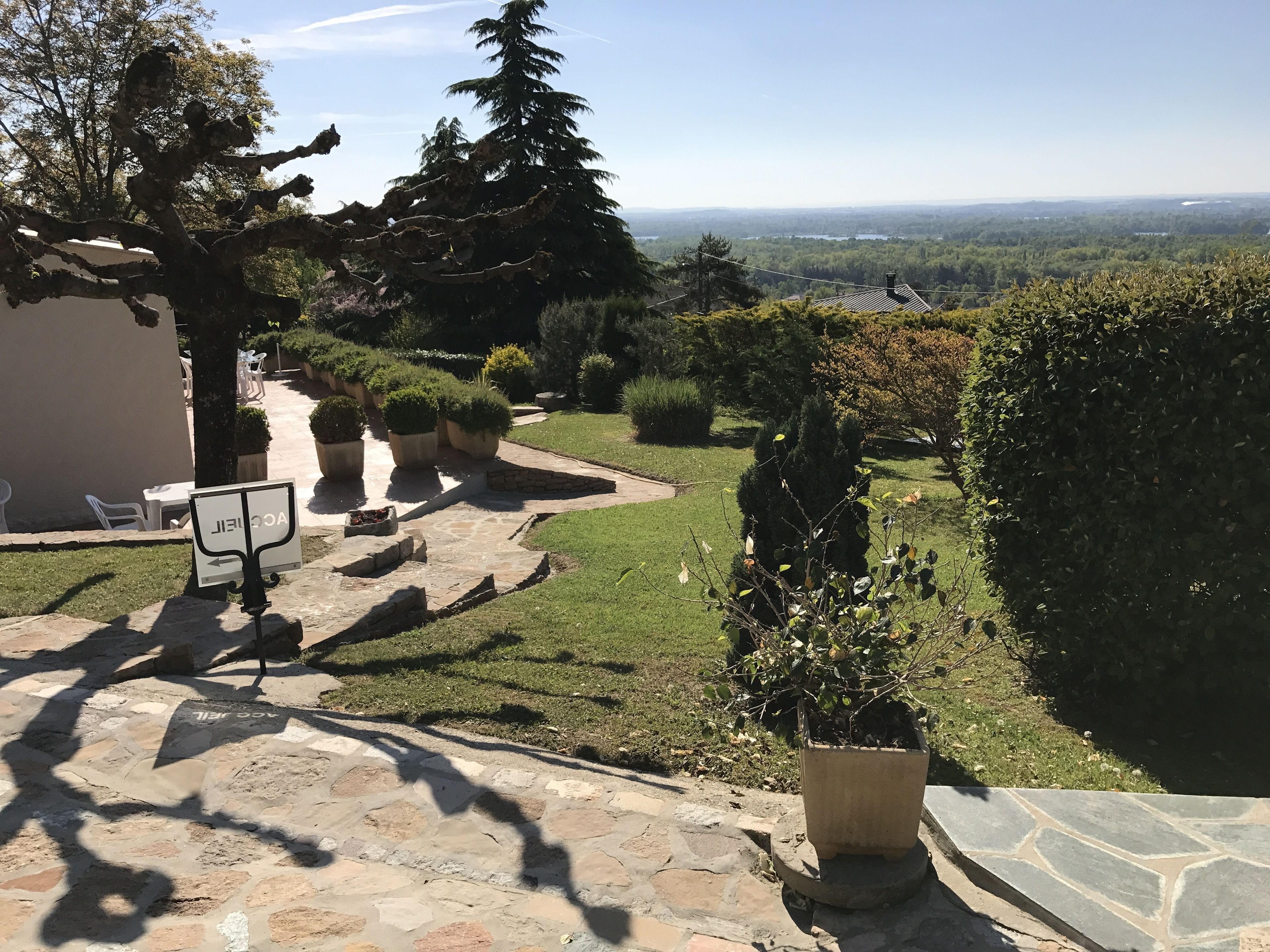 Un sendero de piedra que conduce a un área de estar al aire libre, rodeado de plantas en macetas y una vista de un paisaje lejano.