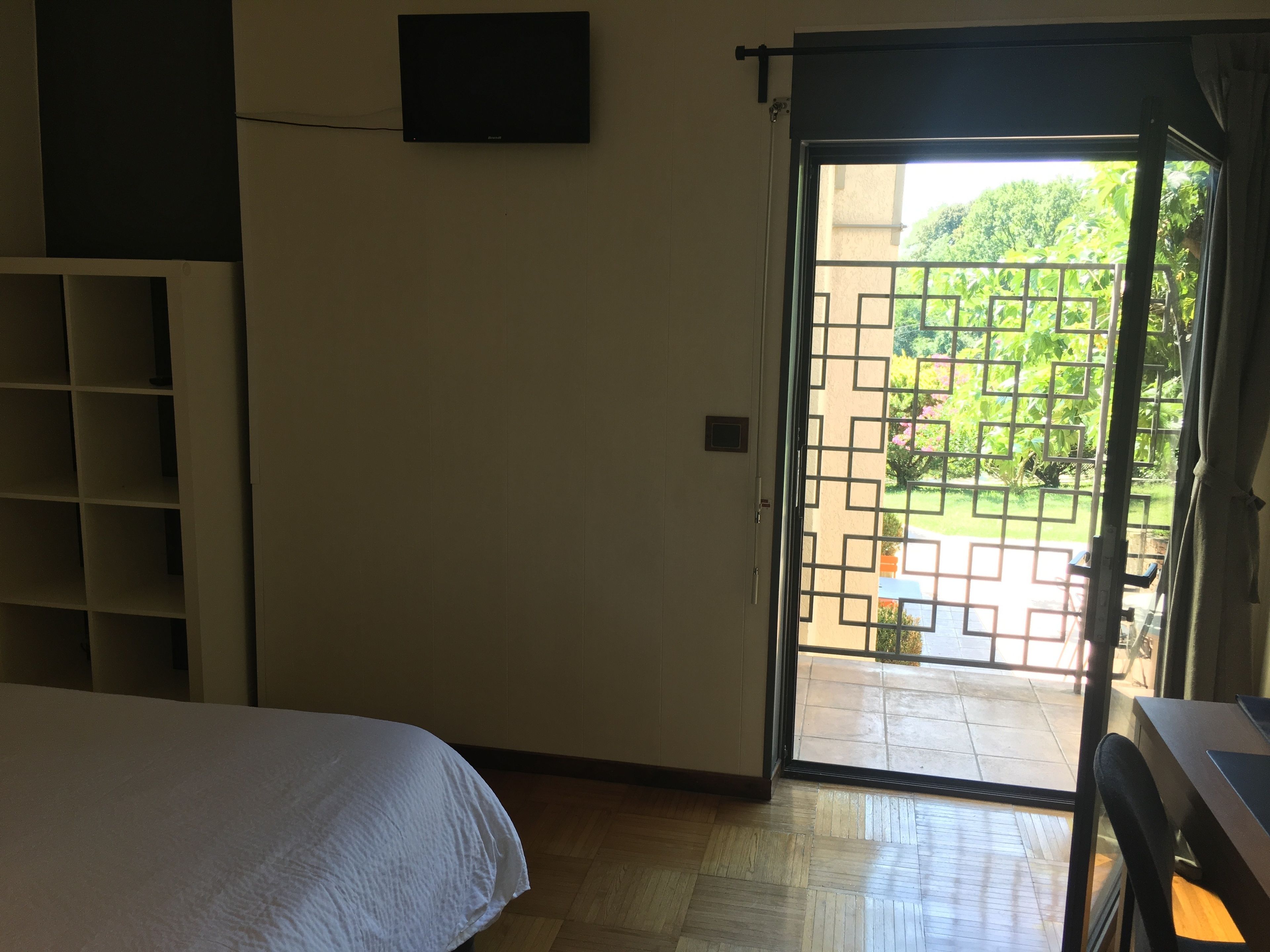 Ein Hotelzimmer mit einem Bett, einem an der Wand befestigten Fernseher und einer Schiebetür zu einem Außenbereich mit Grünblick.