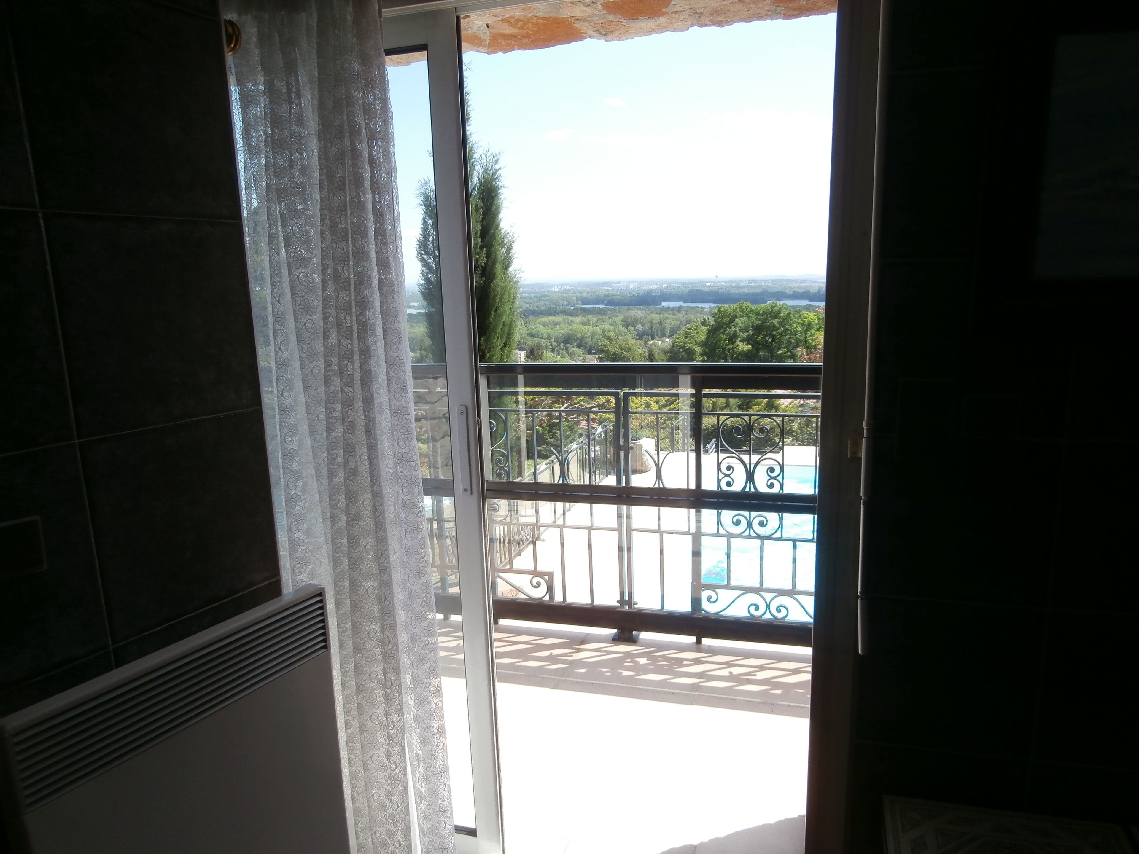 Une vue depuis un balcon donnant sur une piscine, un ciel dégagé et un paysage lointain.