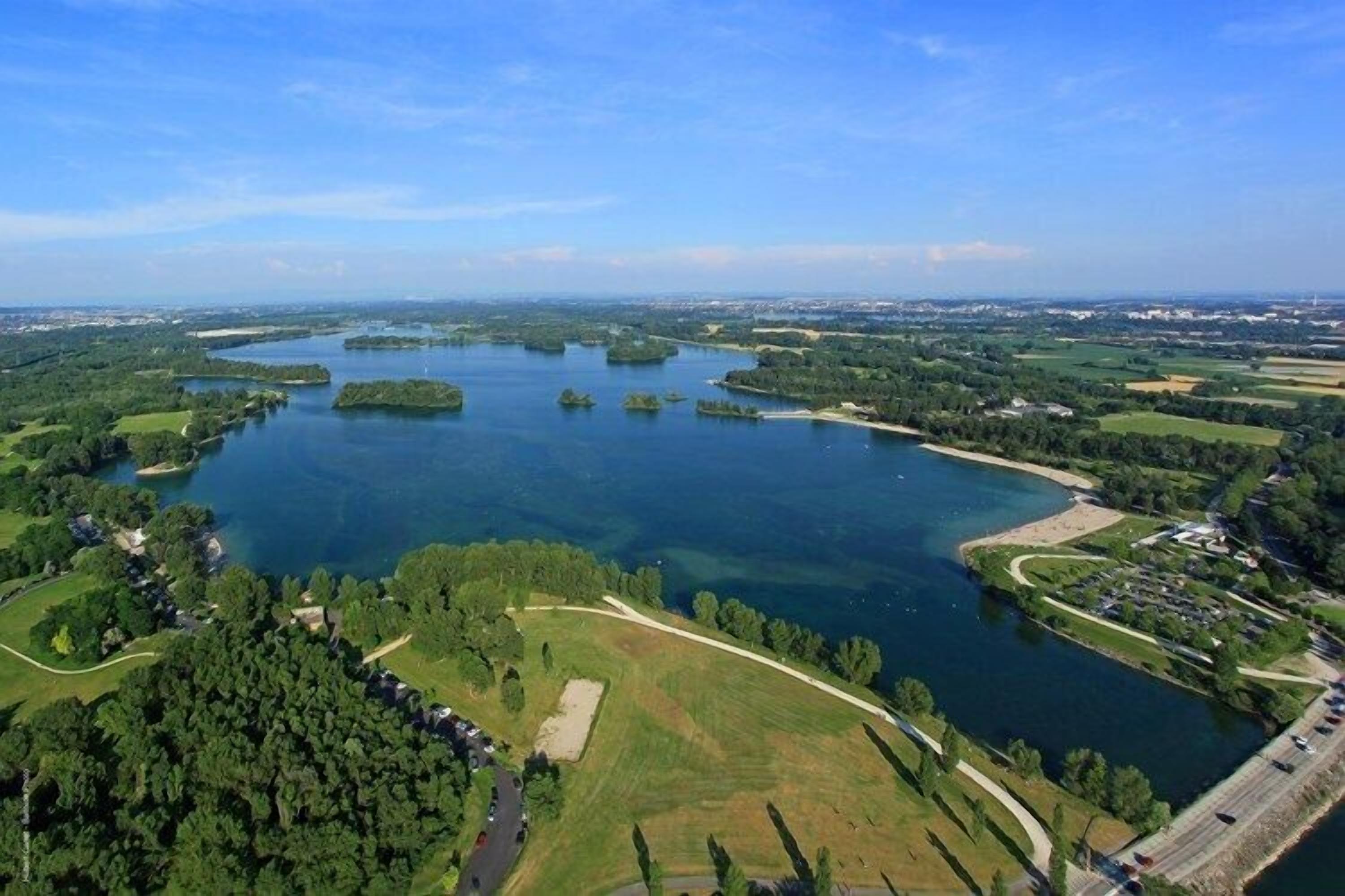 An aerial view of a lake surrounded by greenery and a few buildings.