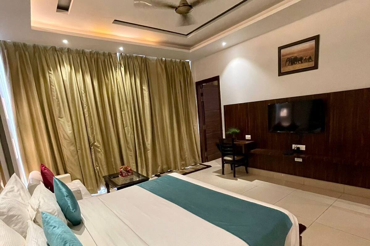 A hotel room with a large bed, a ceiling fan, a TV mounted on the wall, and a window with curtains.