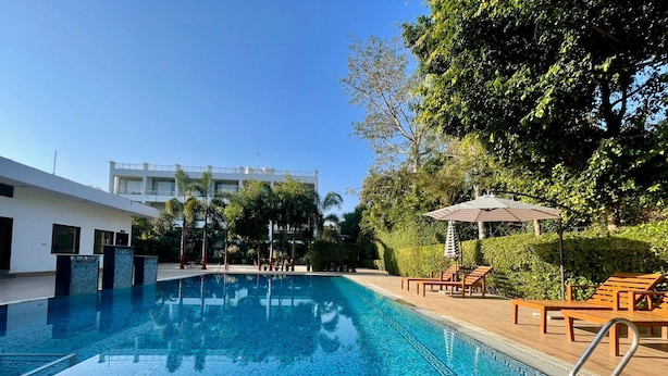 Piscina com padrões em mosaico, rodeada por espreguiçadeiras e guarda-sóis, com um edifício ao fundo.